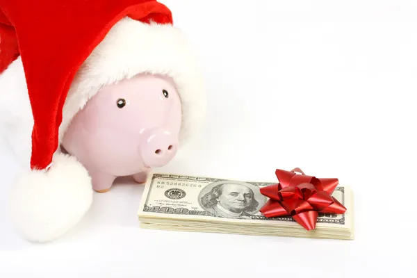 Parte di salvadanaio con cappello di Babbo Natale e mucchio di soldi banconote da cento dollari americani con fiocco rosso su sfondo bianco — Foto Stock