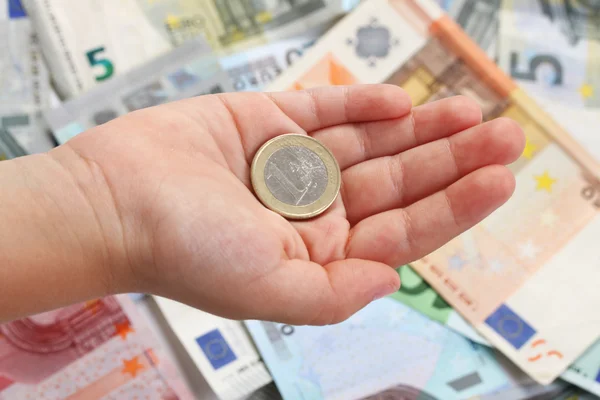 One euro coin on a children's hand on background of euro banknotes — Stock Photo, Image