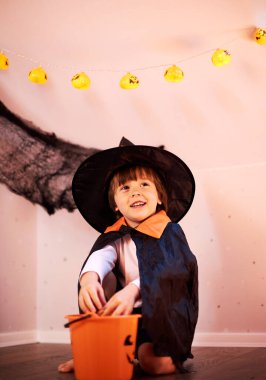  Takım elbiseli ve balkabağı şapkalı tatlı bir çocuk kabak kovasından şeker yiyor..