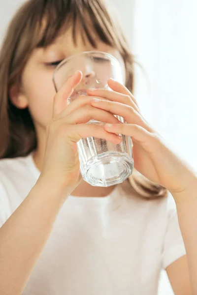 厨房里一个女孩的特写镜头用杯子喝干净的水。把注意力集中在玻璃杯上，面目全非。水对儿童的重要性，保持水的平衡 — 图库照片