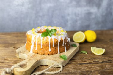 Tahta üzerinde limonlu kek, krema ve limon parçacıklarıyla süslenmiş. Hızlı ve lezzetli bir tatlı.