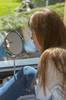 Genç güzel kız pencerenin yanındaki yüzüne makyaj yapar. Aynadaki yansıma, kişisel ve cilt bakımı. Günlük Makyaj