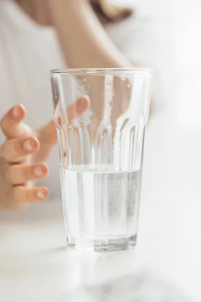 Close-up de um copo meio cheio de água limpa. A criança quer tomar um copo e tomar uma bebida. Água mineral. Foto vertical — Fotografia de Stock