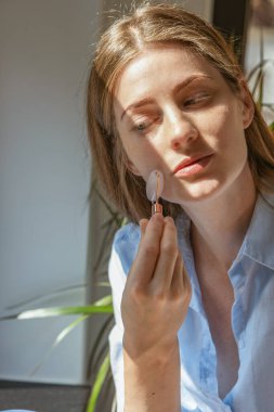 Güzel bir kız evde aynanın önünde bigudiyle yüz masajı yapıyor. Yüz bakımı. Kaldırıyorum. Dikey fotoğraf