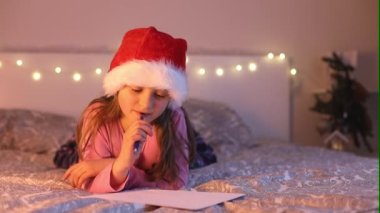 Sana şapkalı şirin bir kız Noel için Noel Baba 'ya dileklerle ve hediyelerle ilgili hayallerle bir mektup yazıyor. Çocukluk hayalleri. Yılbaşı Tatilleri