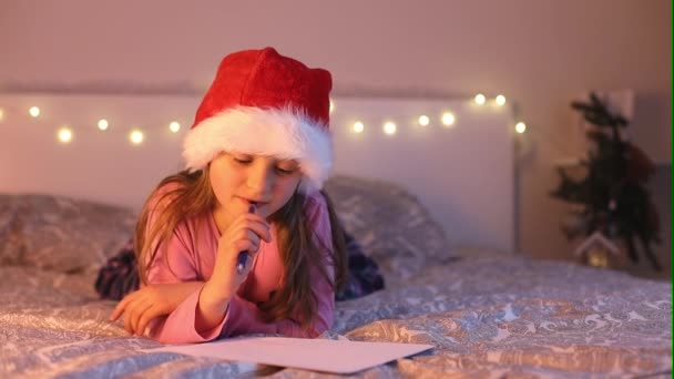 Ein nettes Mädchen mit Sanahut schreibt einen Brief an den Weihnachtsmann mit Wünschen und Träumen von Geschenken. Kindheitsträume. Neujahrsferien — Stockvideo