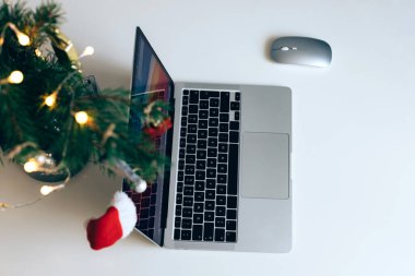 Masada, toplar ve çelenkle süslenmiş bir Noel ağacının yanında açık bir dizüstü bilgisayar. Yeni yıl ve Noel havası. Uzak çalışma ve alışveriş.