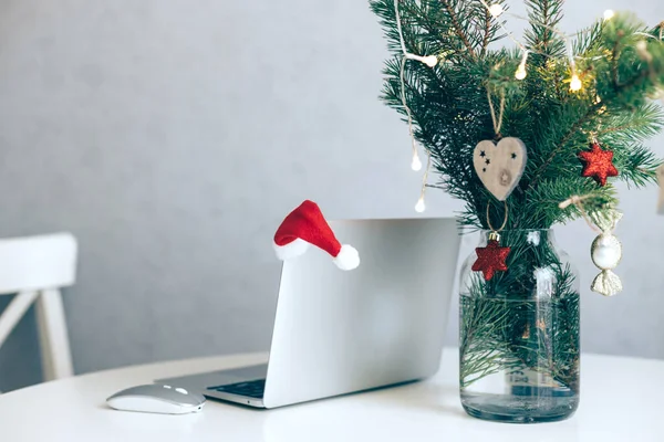 Otevřený notebook na stole vedle vánočního stromku zdobeného míčky a věncem. Nový rok a vánoční nálada na pracovišti — Stock fotografie