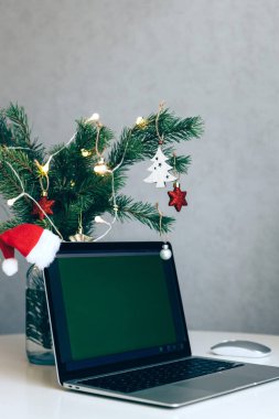 Masada, toplar ve çelenkle süslenmiş bir Noel ağacının yanında açık bir dizüstü bilgisayar. İş yerinde yeni yıl ve Noel havası