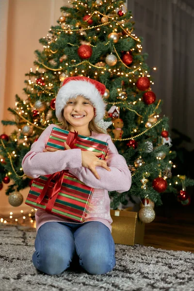 Mutlu yıllar ve mutlu Noeller. Şirin bir kız hediyeyle çok mutlu olur, ona sarılır ve mutlulukla gülümser.