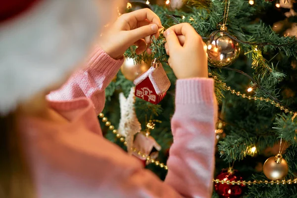 Noel Baba şapkalı bir kızın Noel ağacı oyuncağını Noel ağacında bir eve astığı yakın plan. Mutlu Noeller ve yeni yıl tatilleri
