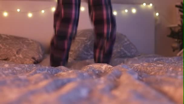 Feliz año nuevo y navidad. Primer plano de pies de chicas adolescentes en pijamas a cuadros saltando sobre la cama. — Vídeos de Stock