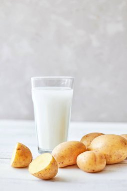Cam bardaktaki patates sütü taze patates odunlarının yanında duruyor. Alternatif bitkisel süt. Gıda trendleri. Vejetaryenler için süt