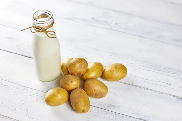 Kartoffelmilch in einer Glasflasche steht neben Kartoffelknollen auf dem Tisch. Alternativ ist pflanzliche Milch ideal für Veganer. Lebensmitteltrends. Kopierraum — Stockfoto