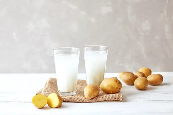 Zwei Gläser Kartoffelmilch auf grauem Hintergrund neben frischen Kartoffelknollen. Alternative Milch. Kräuterdrink für Veganer. Neues Superfood. — Stockfoto