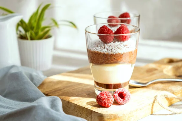 Třívrstvý pěnový dezert z čokolády a vanilky, zdobený čerstvými malinami a kokosovými vločkami ve sklenicích na stole. Brunch, dezert pro milence — Stock fotografie