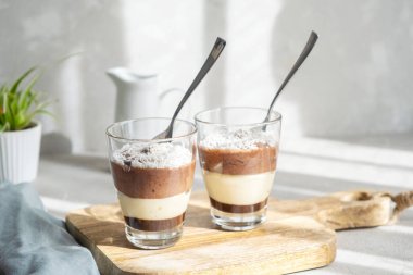 Üç katmanlı çikolata ve cam bardaklarda vanilyalı krema, üzerinde hindistan cevizi taneleri serpiştirilmiş, servis yapan çocuklar için. Kahvaltı.