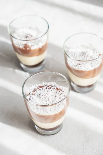 Three-layer chocolate and vanilla mousse dessert in glass cups, sprinkled with coconut flakes, on a childrens serving board. brunch — Stockfoto