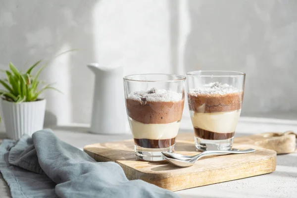 Třívrstvý pěnový dezert z čokolády a vanilky, zdobený čerstvými malinami a kokosovými vločkami ve sklenicích na stole. Brunch, dezert pro milence — Stock fotografie