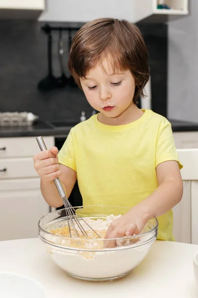 Petit garçon pétrissant la pâte avec un fouet dans la cuisine et souriant. Du temps avec les enfants à la maison. Enfant dans la cuisine. Garçon cuire un cupcake — Photo