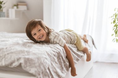 Sevimli çocuk yatağa uzanır, gülümser ve kameraya bakar. Evdeki çocuklar. Dinlenme ve rahatlama.