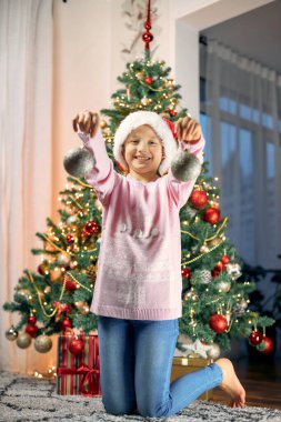 Mutlu Noeller ve yeni yıl tatilleri. Sevimli küçük kız Noel ağacını süslüyor ve Noel süsleriyle oynuyor.