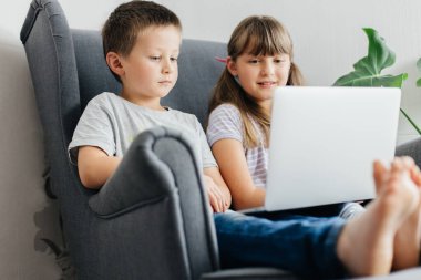 Erkek kardeşiyle birlikte bir liseli kız bir koltukta otururken dizüstü bilgisayarda ders çalışıyor. Çocuklar internetten uzaktan öğreniyorlar. Modern dünyada teknolojinin kullanımı