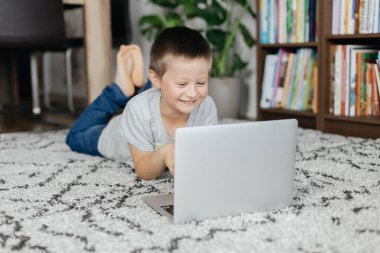 Yakışıklı okul çocuğu yere uzanıyor ve arkadaşlarıyla internette ders izliyor ya da sohbet ediyor. Çocuklar tarafından çevrimiçi öğrenme ve aygıt kullanımı