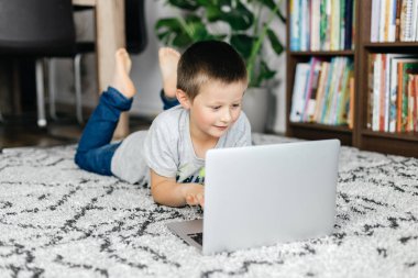 Yakışıklı okul çocuğu yere uzanıyor ve arkadaşlarıyla internette ders izliyor ya da sohbet ediyor. Çocuklar tarafından çevrimiçi öğrenme ve aygıt kullanımı