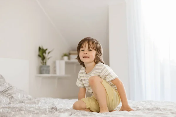 A little boy joyfully jumps on the bed in the bedroom. Fun games at home. Childrens activity and games with parents.