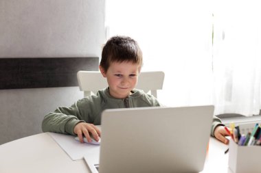 Liseli bir çocuk dizüstü bilgisayarın önünde masaya oturur ve dma öğrenir. Çocuklar için uzaktan öğrenme. Çocuklar alet ve teknoloji kullanır.