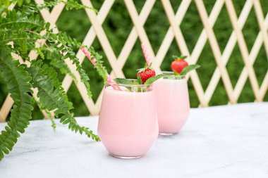 Çilekli smoothie veya muzlu milkshake ve naneli cam bardakta bahçede bir masada. Organik vejetaryen yaz içeceği. Temiz yemek.