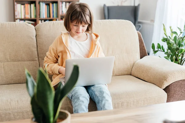 Home schooling for children. A girl sits on a sofa with a laptop on her lap and watches webinars or chats with friends online. Children use technology