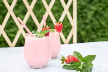 Yazın bahçedeki bir masada cam bardakta naneli süt çilekli muzlu smoothie. Sağlıklı, temiz vejetaryen gıda konsepti. Diyet içki.