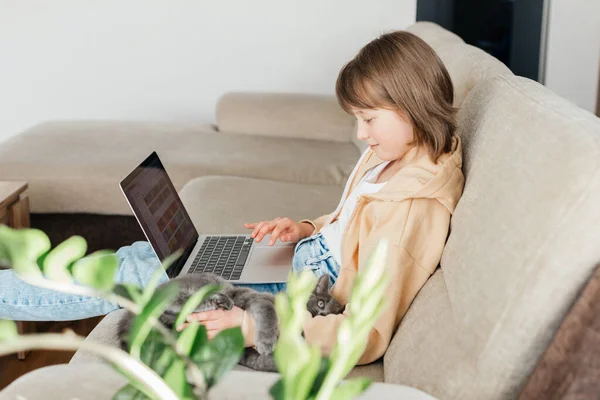 Home schooling for children. A girl sits on a sofa with a laptop on her lap and watches webinars or chats with friends online. Children use technology