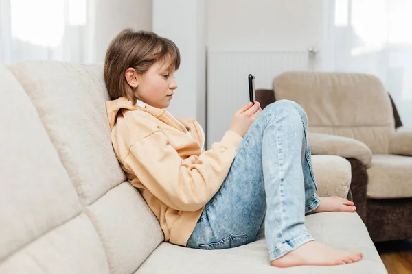 Social media. A schoolgirl girl sits on the couch with a phone in her hands and chats or communicates with friends. Children and gadgets. Young blogger
