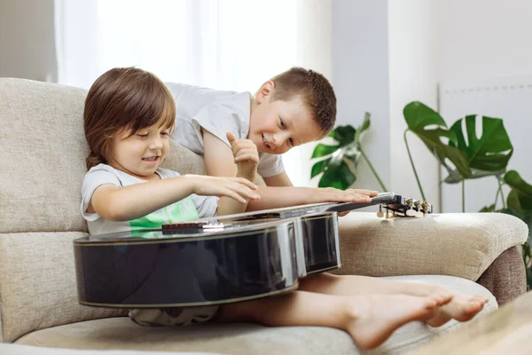 Два Брата Учатся Играть Гитаре Дома Дети Веселятся Дома Диване — стоковое фото
