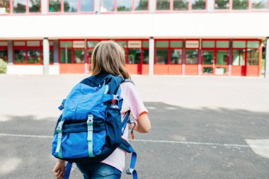 A schoolgirl girl with a school backpack on her back runs to school. Children are excited about the beginning of the school year and are happy to go to classes.