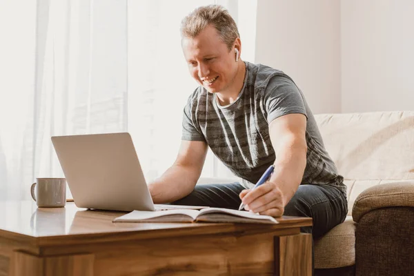A young man studies and works at home with a laptop. Freelancer checks mail, writes letters and uses internet banking services.