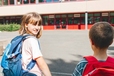 Close-up boy and girl, brother and sister with backpacks on their backs go to school together in an embrace. Beginning of the school year. Children are happy to learn.
