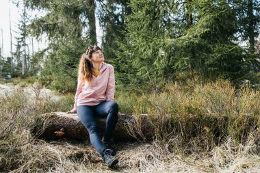 A young beautiful girl sits on a log in the forest and enjoys nature and loneliness. Rest and escape from problems. Rest and replenishment of energy