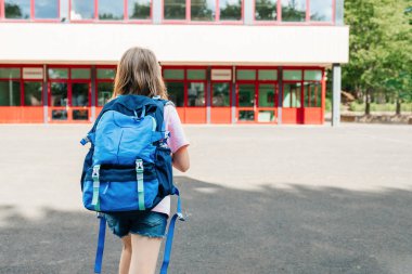 Back view of a schoolgirl with a school backpack on her back going to school. Children are excited about the beginning of the school year and are happy to go to classes. End of vacation.