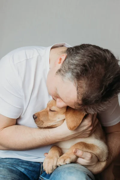 Young man hugging his labrador retriever puppy. The concept of friendship between a dog and a person, care and love for animals. Cute, funny moments of life.