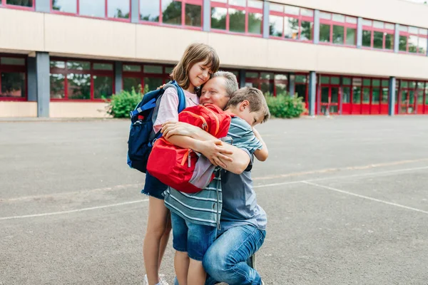 Happy young dad hugging his schoolboy son in front of the school building. Dad takes his child to class. Back to school.