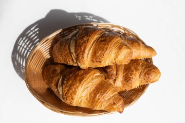 Fresh croissants in a wicker basket in the bright rays of the sun. Fresh pastries for breakfast. Home baking, bakery
