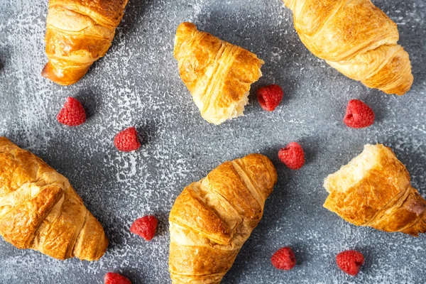 Fresh croissants with raspberries lie on a dark concrete background. View from above. Fresh pastries for breakfast.