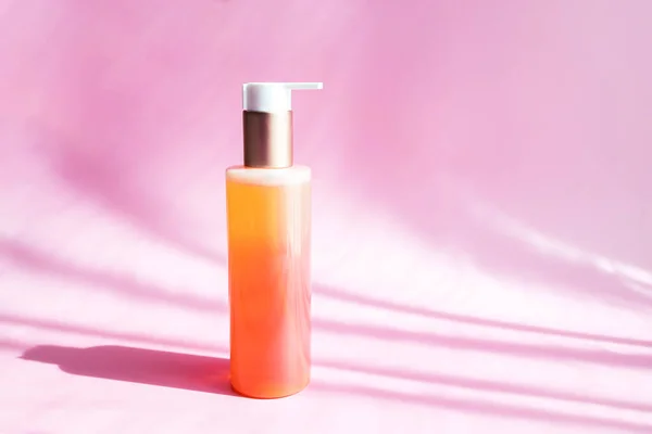 Cosmetic bottle of oil, foam, lotion or body spray on a pink background in the bright rays of the sun with space for text.
