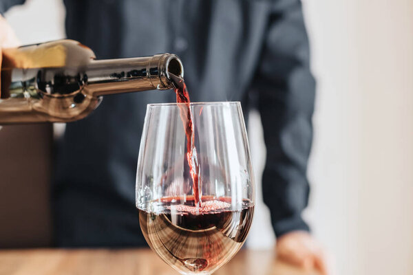 Close-up of a man sommelier pouring red wine from a bottle into a glass.