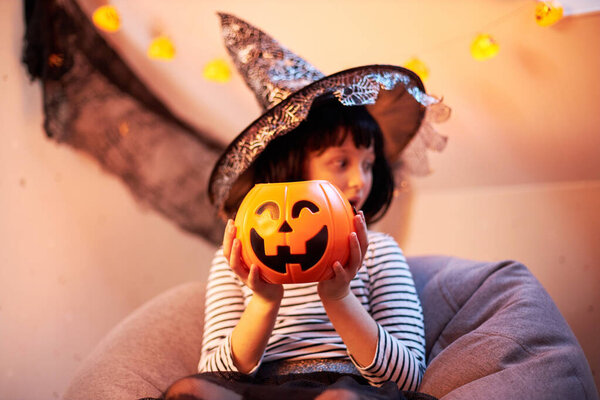 Halloween kids. A cute little girl is sitting with a bucket of pumpkin and a surprised expression on her face. Fun party. Tricks or treats