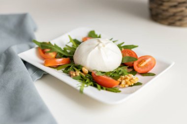 Beyaz servis tabağında roka yapraklı taze burrata peyniri, kiraz domatesleri ve ceviz. Geleneksel İtalyan peyniri. 